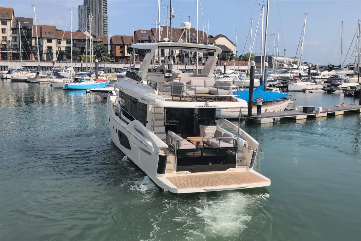 Luxury motor yacht "Absolute" cruising in a marina with various boats and modern buildings in the background.